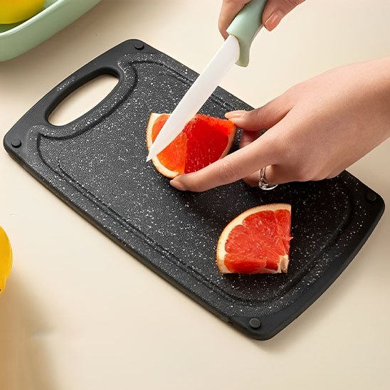 Planche à découper Duralite Premium taille petite vue de haut montrant une femme qui tranche une orange sanguine avec un économe