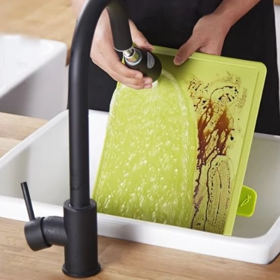 Planche à découper coloricone verte passée sous un robinet de cuisine moderne