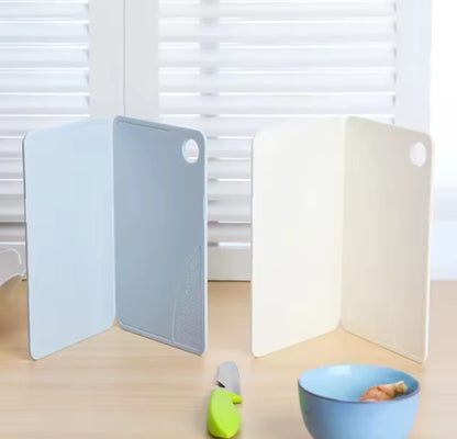 Démonstration du duo de planches à découper ouvertes à 90 degrés déposées sur une table en bois clair, avec un petit bol bleu et un couteau couleur lime à l'avant plan