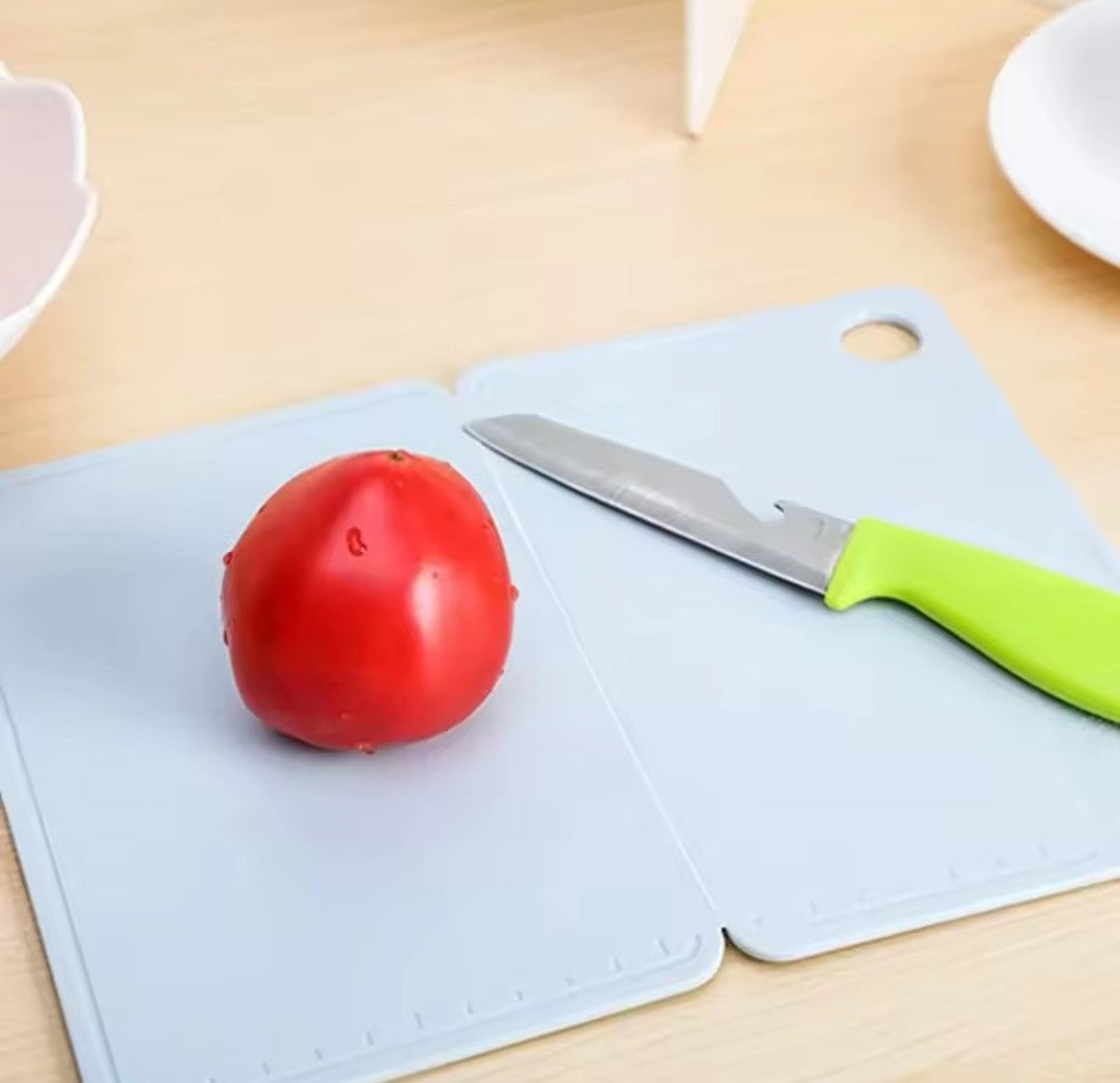 Démonstration de la planche à découper bleue claire ouverte en deux, sur laquelle il y a une tomate ronde et un petit couteau à manche vert lime