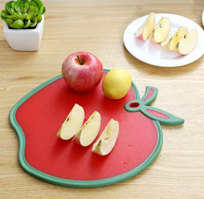 Présentation de la planche à découper en forme de pomme, sur laquelle il y a une pomme en quartiers, ne pomme ronde et un citron