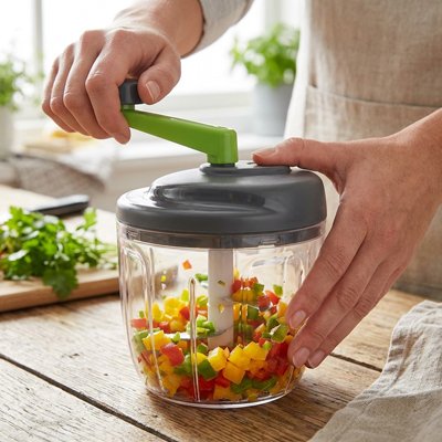 Hachoir manuel rotatif présenté par quelqu'un qui tourne la manivelle pour hacher des légumes colorés
