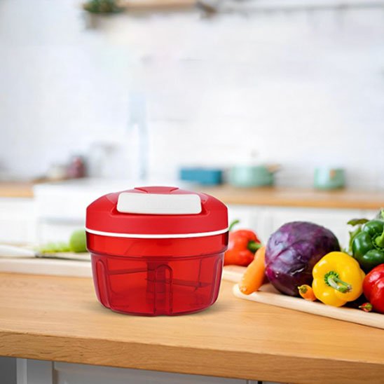 Présentation du hachoir manuel rouge transparent vide, sur un comptoir en bois entouré de légumes