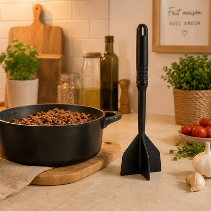 Hachoir à viande manuel noir à 4 pales posé sur un comptoir près d'une casserole de viande hachée dans une cuisine moderne.