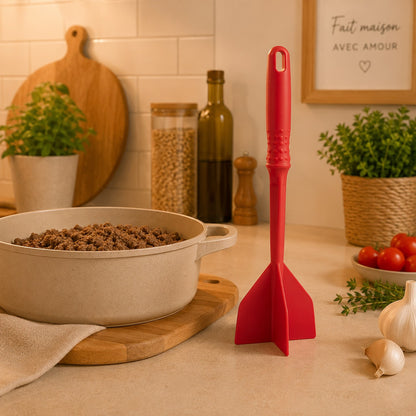 Hachoir à viande manuel rouge à 4 pales posé sur un comptoir près d'une casserole de viande hachée dans une cuisine moderne.