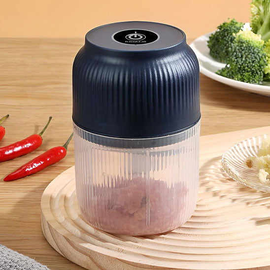 Mini hachoir USB au couvercle-moteur noir et base semi transparente présenté sur planche en bois et table en bois, entouré de brocoli et piment rouge