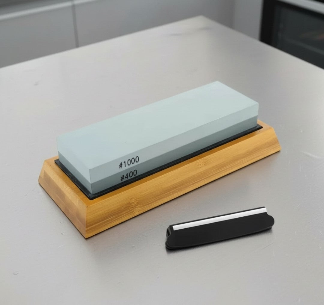 L'ensemble pierre à aiguiser quatre pièces comprend: une pierre double face #400 et #1000, un ajusteur d'angles, une base mince en silicone qui elle vient s'insérer dans une jolie base en bambou pour une meilleur préhension. L'ensemble est présenté sur un joli comptoir de cuisine en inox.