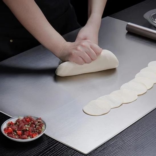 Planche à découper professionnelle en inox sur laquelle un chef pétri de la pâte