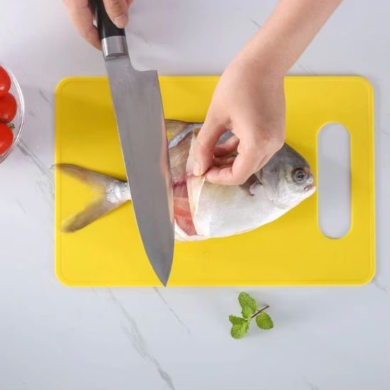 Planche à découper DayliCut jaune vue de haut, démontrant une femme qui pèle la peau d'un tilapia