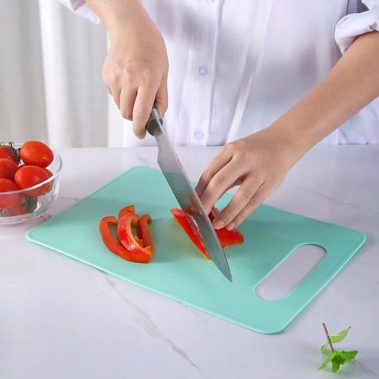 Planche à découper DayliCut de couleur turquoise montrant un cuistot qui coupe des lamelles de poivron rouge