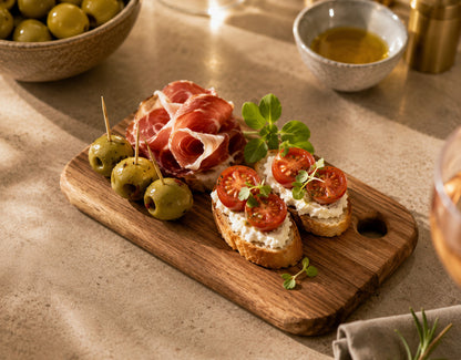 Petite planche en bois d'acacia garnie de tapas, bruschettas, olives et jambon cru, idéale pour l'apéritif.