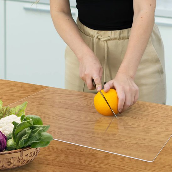 Planche à découper en acrylique clair montrant une femme qui tranche une orange en deux