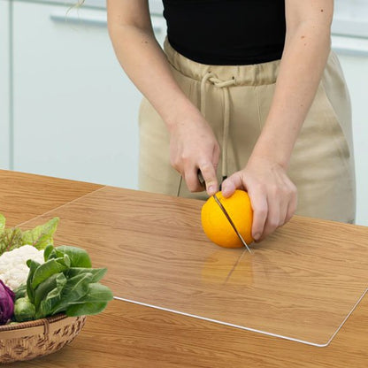 Planche à découper en acrylique clair montrant une femme qui tranche une orange en deux