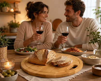 Couple partageant un repas romantique avec une planche à découper ronde en bambou garnie d'une miche de pain et de tranches fraîches au centre de la table.