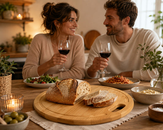 Couple partageant un repas romantique avec une planche à découper ronde en bambou garnie d'une miche de pain et de tranches fraîches au centre de la table.