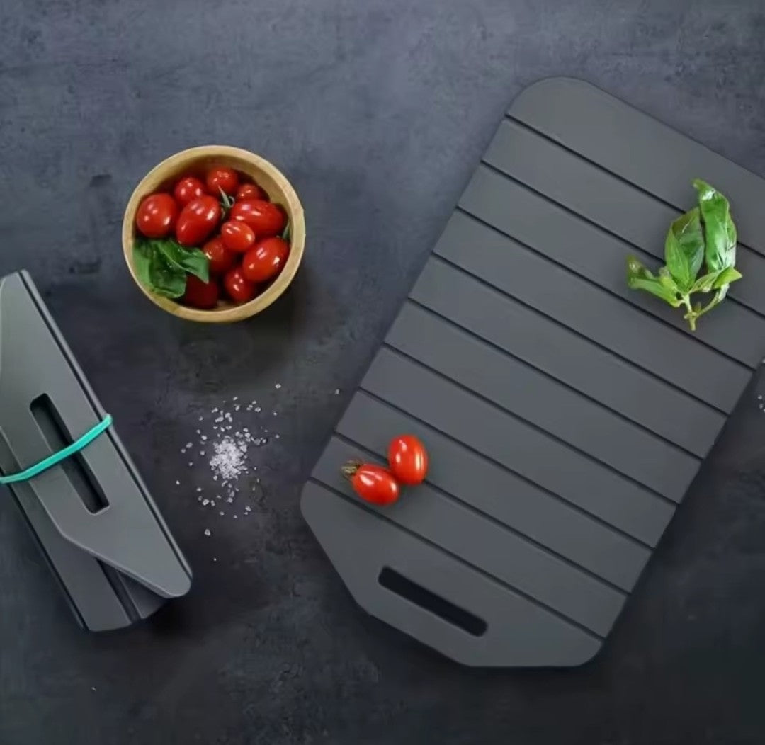 Présentation chic de la planche à désouper grise vue de haut sur table en marbre noir mat avec un bol de tomates cerises, quelques grains de gros set et une feuille de basilic