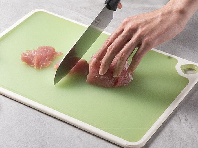 Image de près montrant une femme qui tranche un poulet sur sa planche à découper antibactérienne