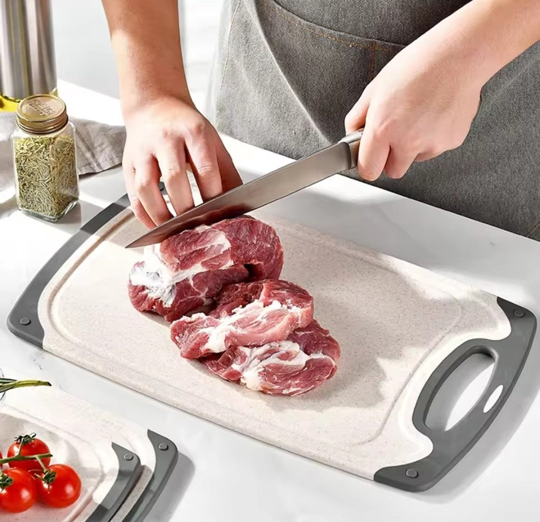 Jeune chef en train de tranche une pièce de viande sur une planche à découper de taille moyenne aux contours de silicone gris.
