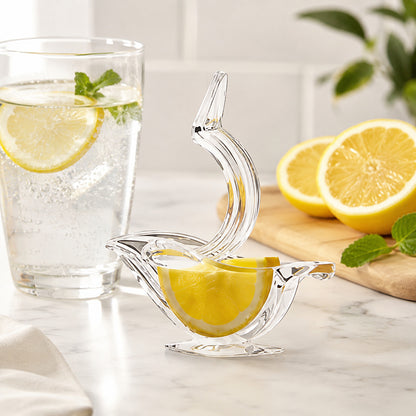 Joli presse agrume en acrylique clair en forme d'oiseau dans lequel il y a une demie tranche de citron, entouré d'un verre d'eau pétillante et un citron coupé en 2 sur une planche à découper.