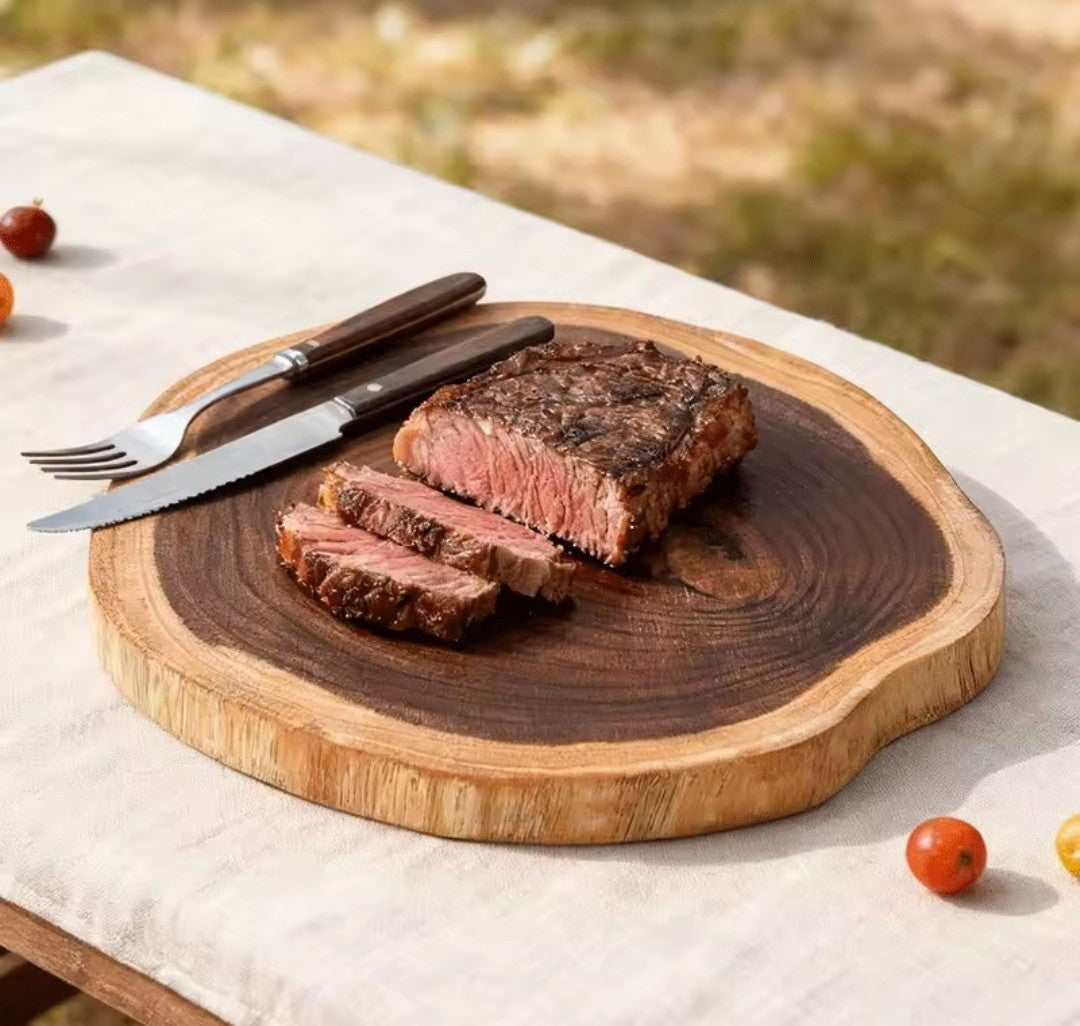 Présentation de la planche à découper en forme de tronc tranché transversalement, sur laquelle il y a un steak tranché et un couvert.
