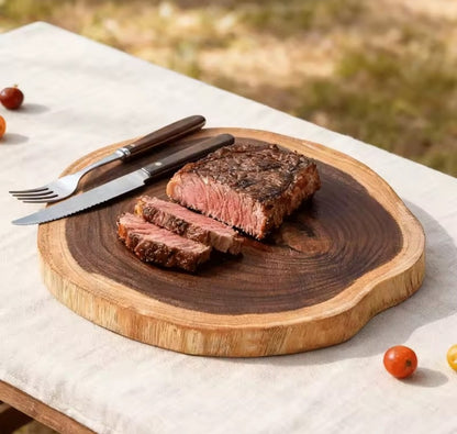 Présentation de la planche à découper en forme de tronc tranché transversalement, sur laquelle il y a un steak tranché et un couvert.